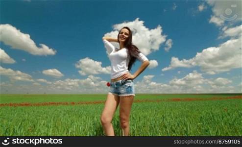 Attractive young woman posing for the camera and walks away on a green field of wheat