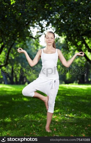 Attractive young woman practices yoga in the park