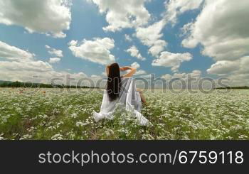 Attractive young woman sitting in a white blossoming field with her arms spread widely