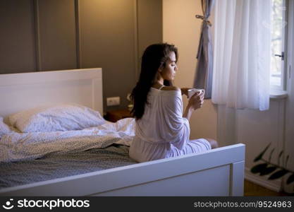 Attractive young woman sitting on a bed with mug in bedroom