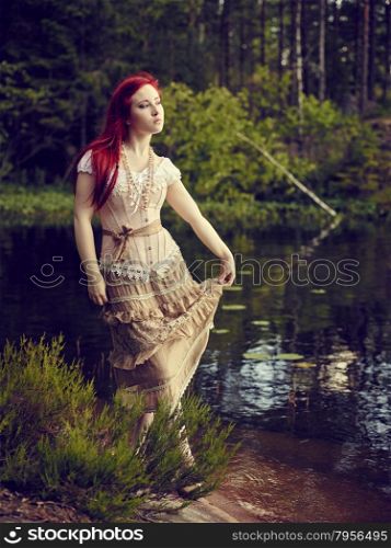 Attractive young woman wearing a dress and she standing beside waterline, lake on background