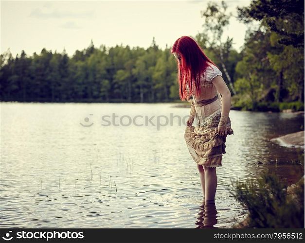 Attractive young woman wearing a dress and she standing on waterline, summer day on the lake