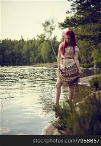 Attractive young woman wearing a dress and she standing on waterline, summer day on the lake