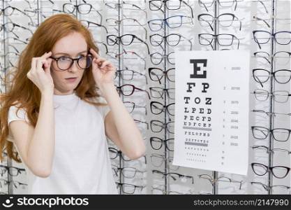 attractive young woman wearing eyeglasses standing neat snellen chart optica