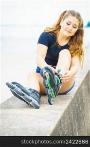 Attractive young woman wearing rol≤r skates relaxing after ride. Fema≤being sporty having fun during∑mer time on sea coast.. Girl wearing rol≤r skates on seaside