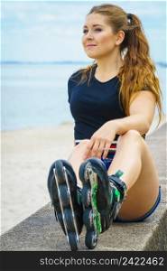 Attractive young woman wearing roller skates relaxing after ride. Female being sporty having fun during summer time on sea coast.. Girl wearing roller skates on seaside