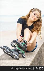 Attractive young woman wearing roller skates relaxing after ride. Female being sporty having fun during summer time on sea coast.. Girl wearing roller skates on seaside