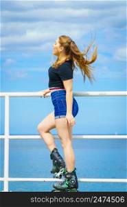 Attractive young woman wearing roller skates relaxing after ride. Fit female having fun during summer time on sea coast.. Girl wearing roller skates on seaside