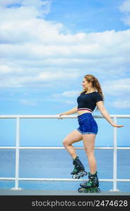 Attractive young woman wearing roller skates relaxing after ride. Fit female having fun during summer time on sea coast.. Girl wearing roller skates on seaside