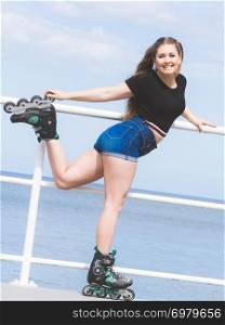 Attractive young woman wearing roller skates relaxing after ride. Fit female having fun during summer time on sea coast.. Girl wearing roller skates on seaside