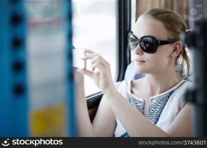 Attractive young woman wearing sunglasses holding up and photographing at her mobile on a bus or train