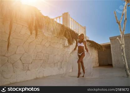 Attractive young woman wearing swimsuit and pareo standing over white bamboo wall.. Attractive young woman wearing swimsuit and pareo standing over white bamboo wall