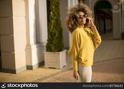 Attractive young woman with curly hair using her touch screen mobile cell phone on the street