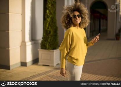Attractive young woman with curly hair using her touch screen mobile cell phone on the street
