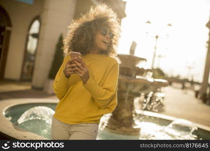 Attractive young woman with curly hair using her touch screen mobile cell phone by the fountain