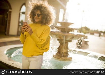 Attractive young woman with curly hair using her touch screen mobile cell phone by the fountain