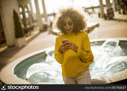 Attractive young woman with curly hair using her touch screen mobile cell phone by the fountain