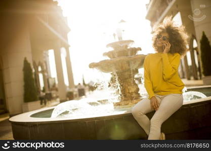 Attractive young woman with curly hair using her touch screen mobile cell phone by the fountain