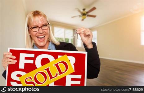 Attractive Young Woman with New Keys and Sold Real Estate Sign In Empty Room of House.