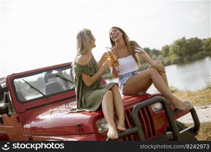Attractive young women having fun and sitting on a convertible car by river