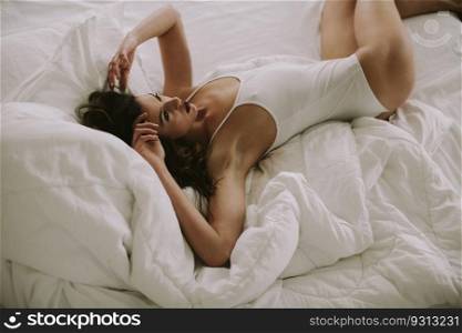 Attracttive young woman lies in white bed