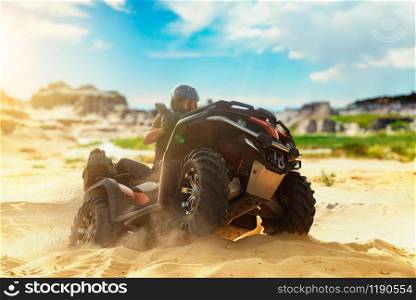 Atv freeriding in sand quarry, extreme sport. Male driver in helmet riding on quad bike in sandpit