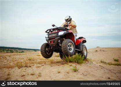 Atv racer in helmet, downhill riding in desert sands, action view. Male person on quad bike, sandy race, dune safari in hot sunny day, 4x4 extreme adventure, quad-biking. Atv racer in helmet riding in desert, action view