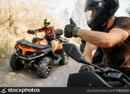 ATV rider in helmet showing thumbs up to his partner, offroad trip in the forest. Riding on quad bike, extreme sport and travelling, quadbike adventure. ATV rider showing thumbs up to his partner