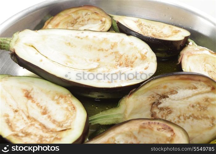 Aubergine or eggplant halves in a frying pan with olive oil