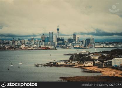 Auckland city skyline, New Zealand, with fishing wharf, city center and Auckland Sky Tower in cloudy day. Vintage color filter.