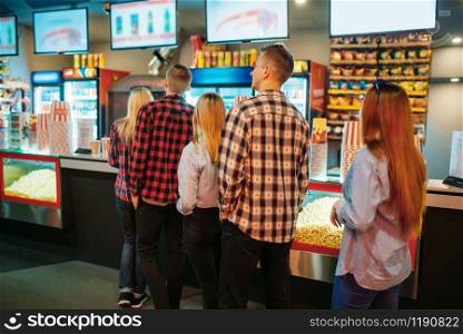 Audience choosing food in cinema bar before the showtime, back view. Male and female youth in movie theater