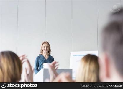 Audience clapping for smiling businesswoman in office conference