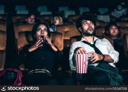 Audience sitting in a cinema and watching terrible horror. Afraid woman sitting near a man is shock and scare