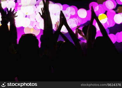 Audience watching a rock show, hands in the air, rear view, stage lights