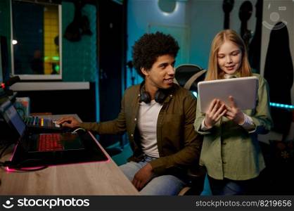 Audio engineer with young girl singer working in music recording studio using mobile digital tablet. Audio engineer with young singer working in music recording studio