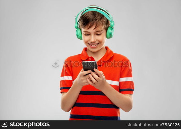 audio equipment and technology people concept - happy smiling boy in headphones listening to music on smartphone over grey background. boy in headphones listening to music on smartphone