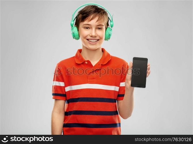 audio equipment and technology people concept - happy smiling boy in headphones listening to music on smartphone over grey background. boy in headphones listening to music on smartphone