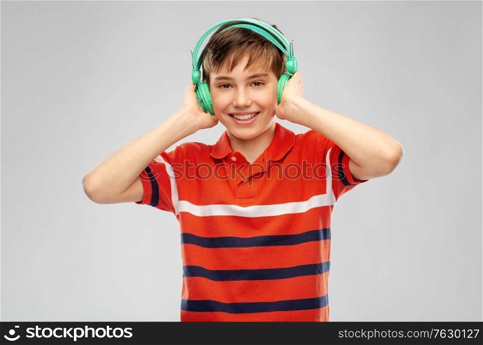 audio equipment and technology people concept - happy smiling boy in headphones listening to music over grey background. smiling boy in headphones listening to music