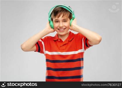 audio equipment and technology people concept - happy smiling boy in headphones listening to music over grey background. smiling boy in headphones listening to music