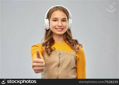 audio equipment and technology people concept - smiling teenage girl in headphones listening to music and showing thumbs up over grey background. teenage girl in headphones showing thumbs up