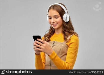 audio equipment and technology people concept - smiling teenage girl in headphones listening to music on smartphone over grey background. teenage girl in headphones listening to music
