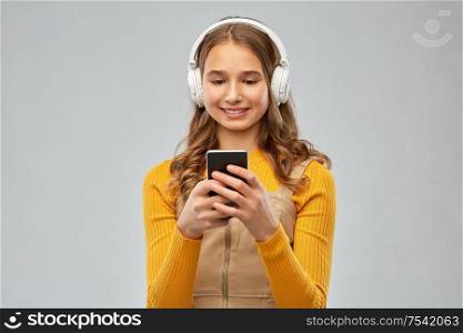 audio equipment and technology people concept - smiling teenage girl in headphones listening to music on smartphone over grey background. teenage girl in headphones listening to music