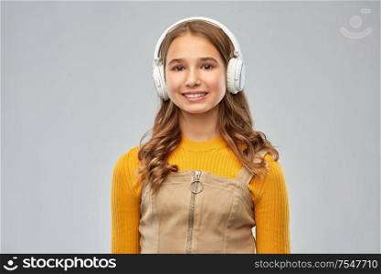audio equipment and technology people concept - smiling teenage girl in headphones listening to music over grey background. teenage girl in headphones listening to music