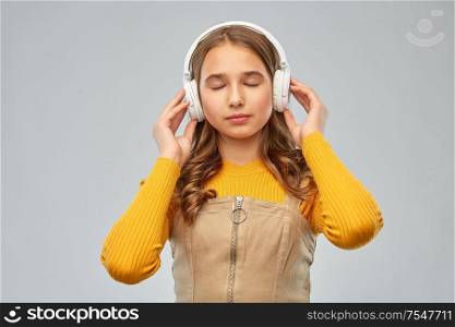 audio equipment and technology people concept - smiling teenage girl in headphones listening relaxing music over grey background. teen girl in headphones listening relaxing music