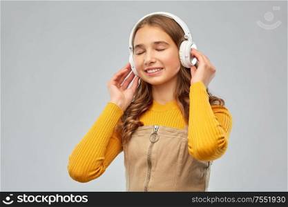 audio equipment and technology people concept - smiling teenage girl in headphones listening to music over grey background. teenage girl in headphones listening to music
