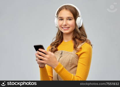 audio equipment and technology people concept - smiling teenage girl in headphones listening to music on smartphone over grey background. teenage girl in headphones listening to music