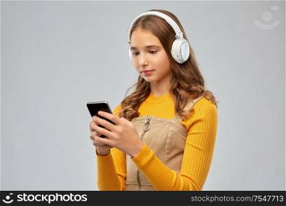audio equipment and technology people concept - teenage girl in headphones listening to music on smartphone over grey background. teenage girl in headphones listening to music