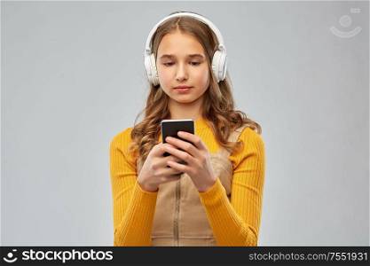 audio equipment and technology people concept - teenage girl in headphones listening to music on smartphone over grey background. teenage girl in headphones listening to music