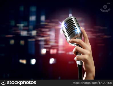 audio microphone retro style. Female hand holding a single retro microphone against colourful background