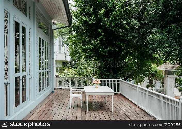 AUG 4, 2014 Bangkok, Thailand - Oriental Thai vintage furniture, white wood chair and table at old house garden balcony with wood floor, natural light and big tree